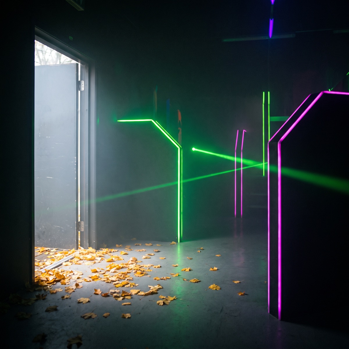 Lasertag-Arena mit Neonlicht, durch die offene TÃ¼r fÃ¤llt Herbstlicht und Laub